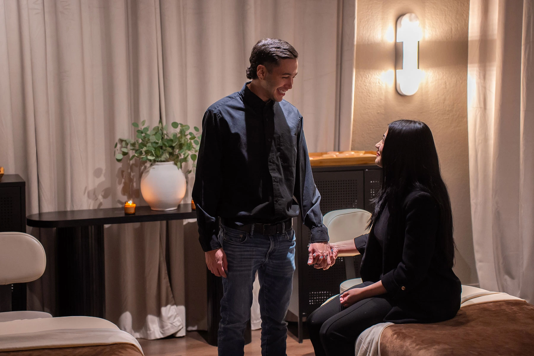 A couple holding hands, with one guest seated in a Zen'd Out treatment suite